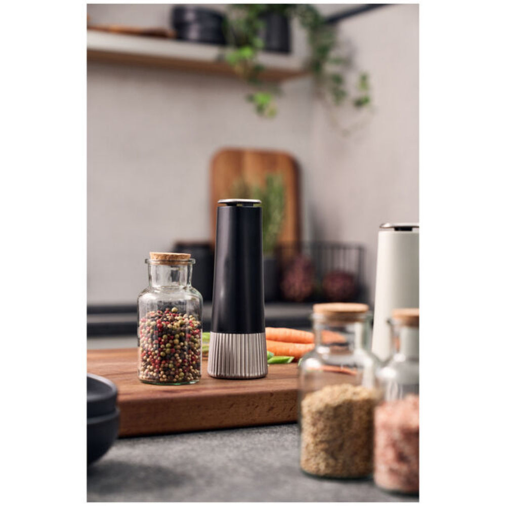 Black pepper grinder on a kitchen counter with jars of spices