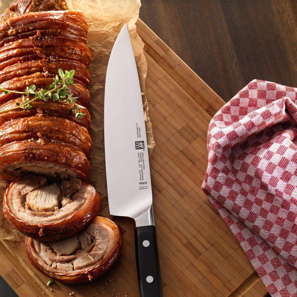 Sliced roasted pork with a knife on a wooden cutting board, next to a red and white checkered towel.
