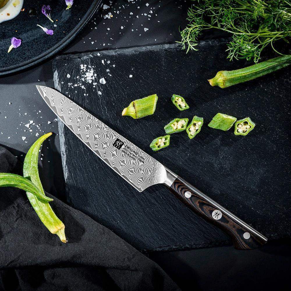Damascus knife on a black surface with okra and herbs