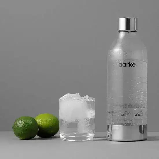 Aarke polished steel water bottle with sparkling water, glass with ice, and two limes, Cookin Stores kitchenware