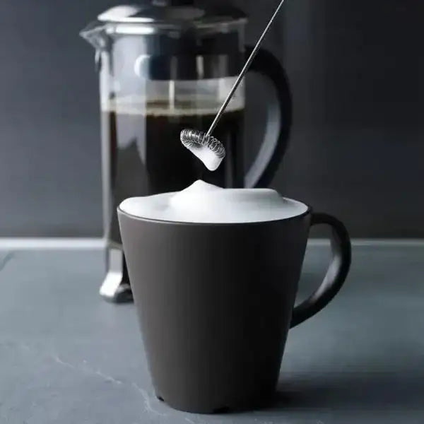 Black mug with frothed milk being poured, French press in the background