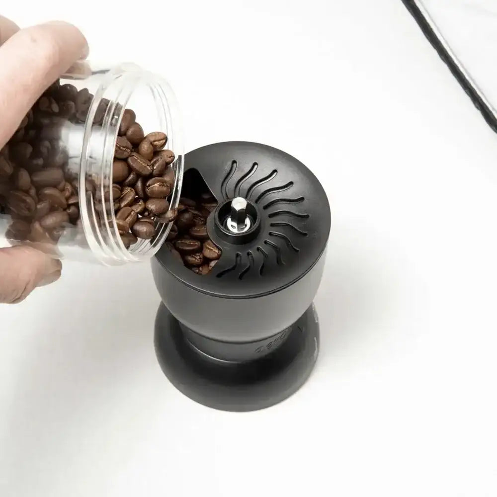 Black coffee grinder with a container of coffee beans on a white background