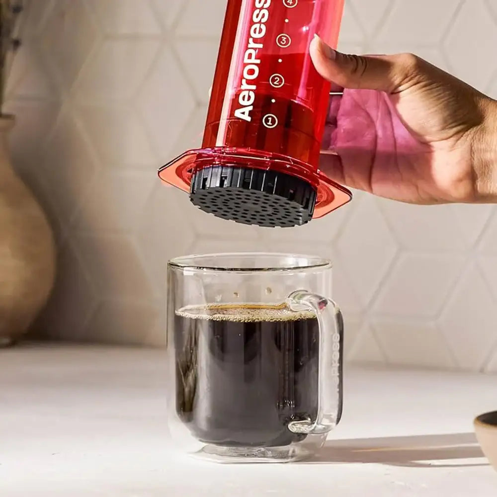 A person using an Aeropress to make coffee in a glass mug.