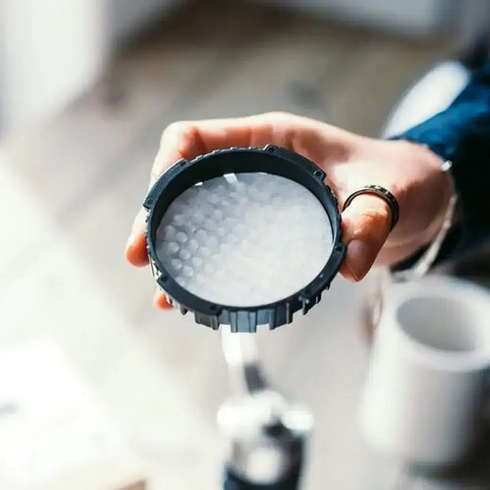 Hand holding a black coffee filter with coffee grounds inside, blurred kitchen background