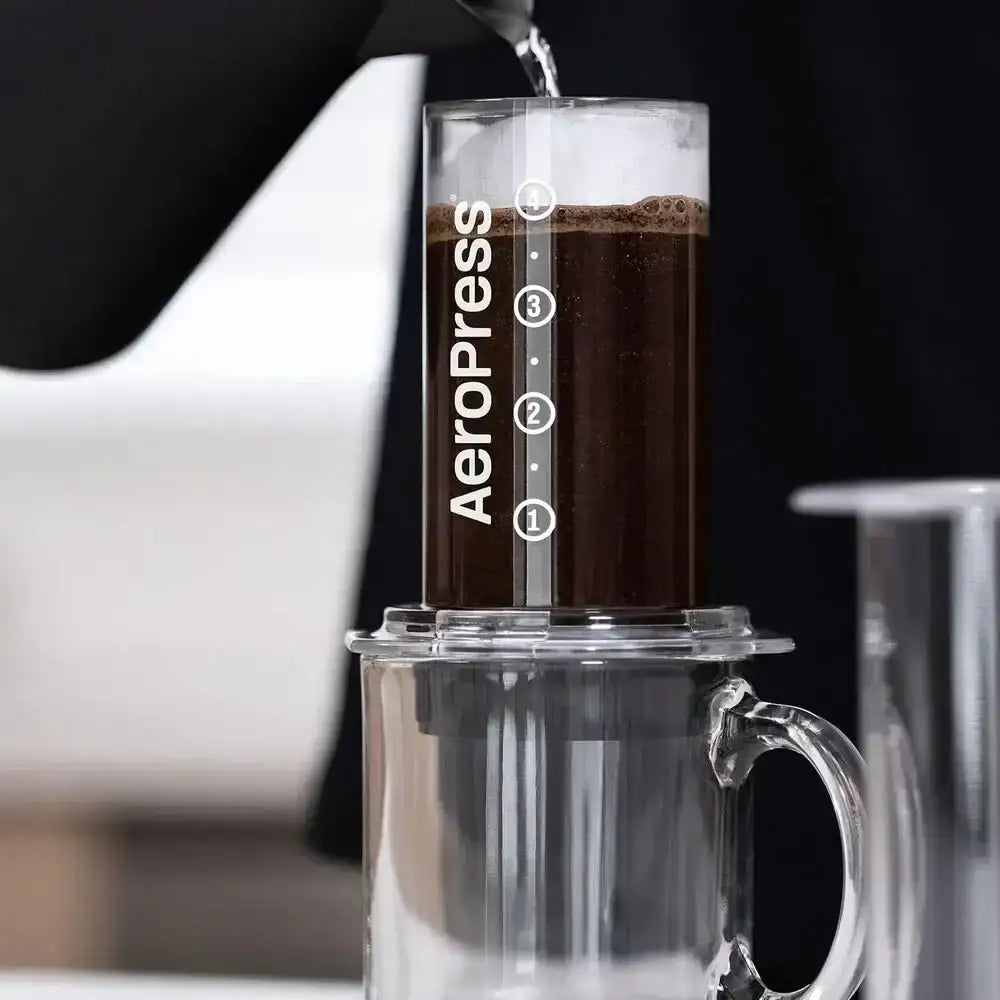Aeropress coffee maker with coffee being poured into it against a black background