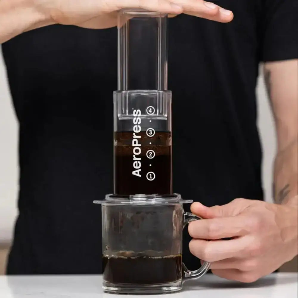 Person using an Aeropress to make coffee with a clear container below.