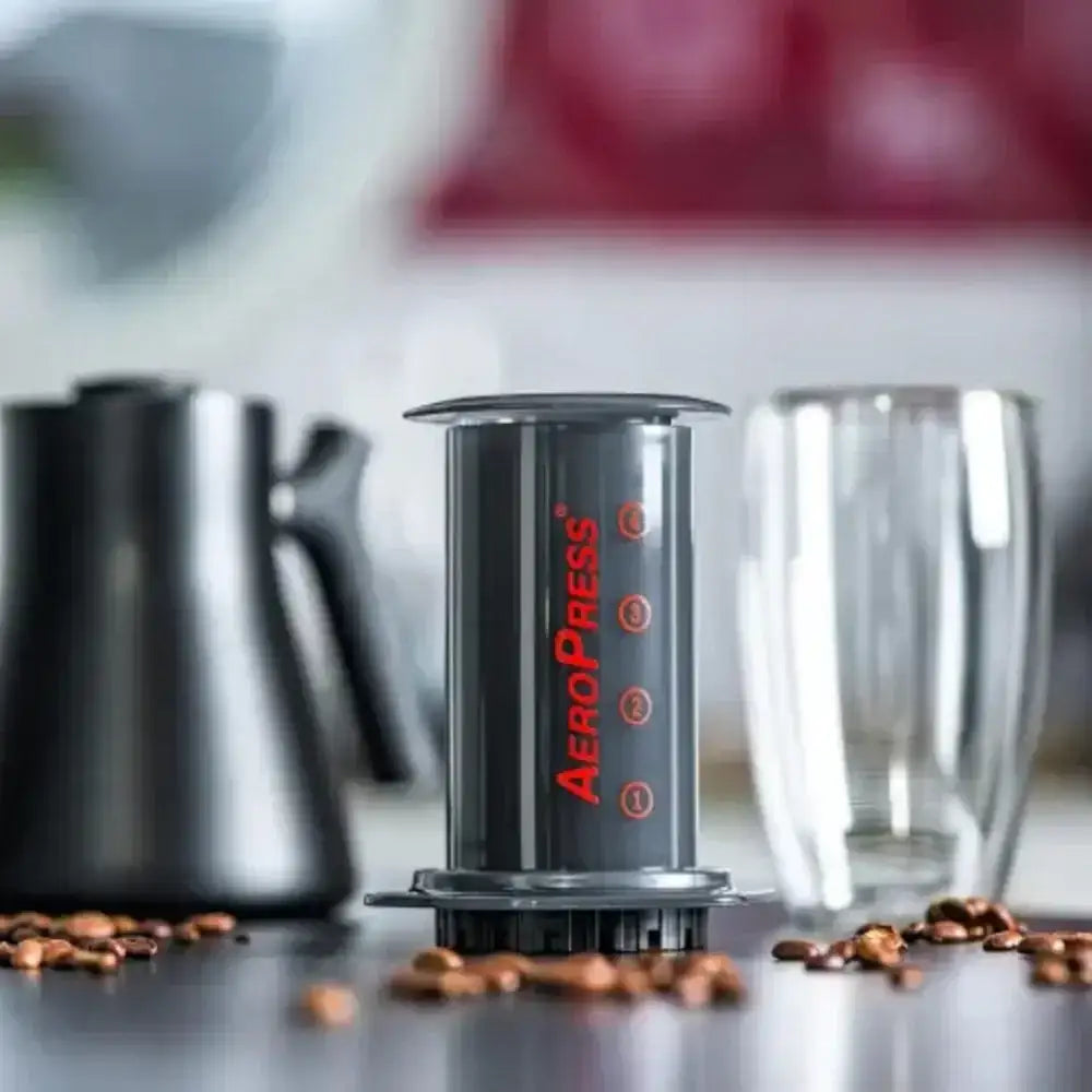 Aeropress coffee maker on a kitchen counter with coffee beans and a glass.