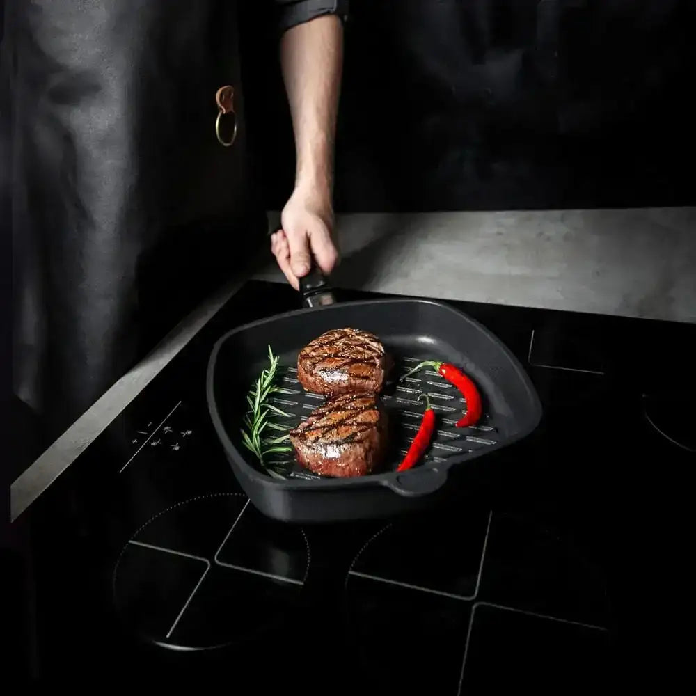 Non-stick square BBQ grill pan with grilled steaks, rosemary, and chili on stovetop at Cookin Stores