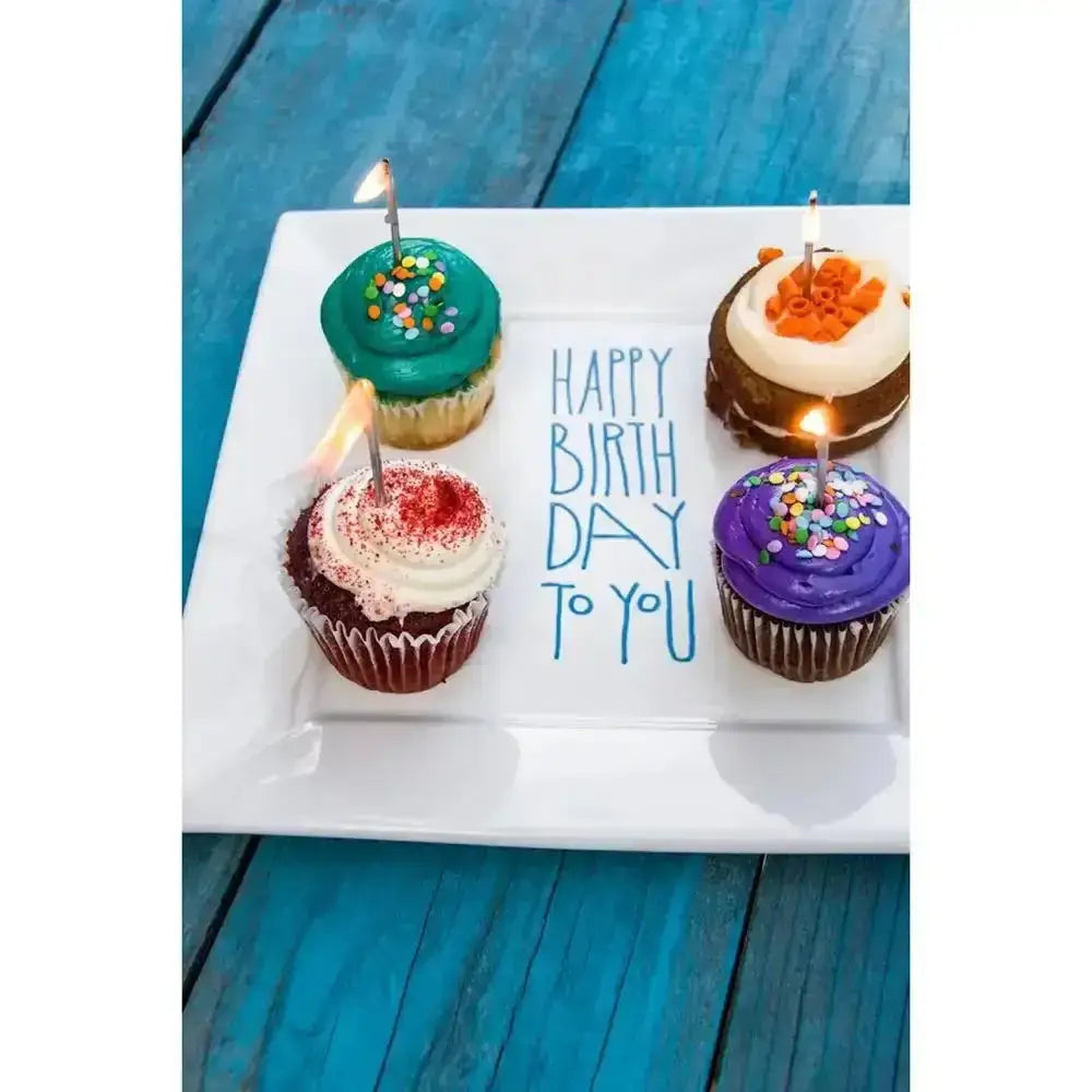 Colorful cupcakes with candles on a white plate against a blue wooden background