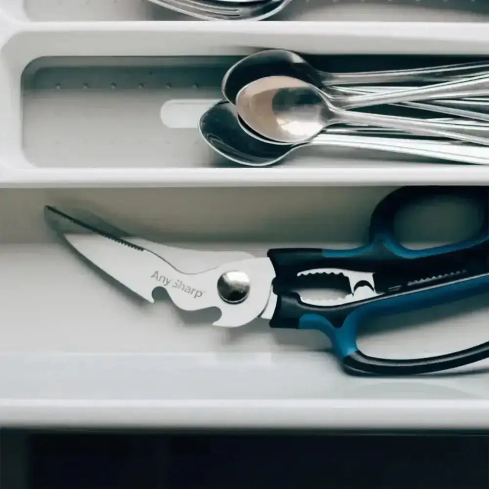 Set of scissors and knives on a white tray with cutlery in the background