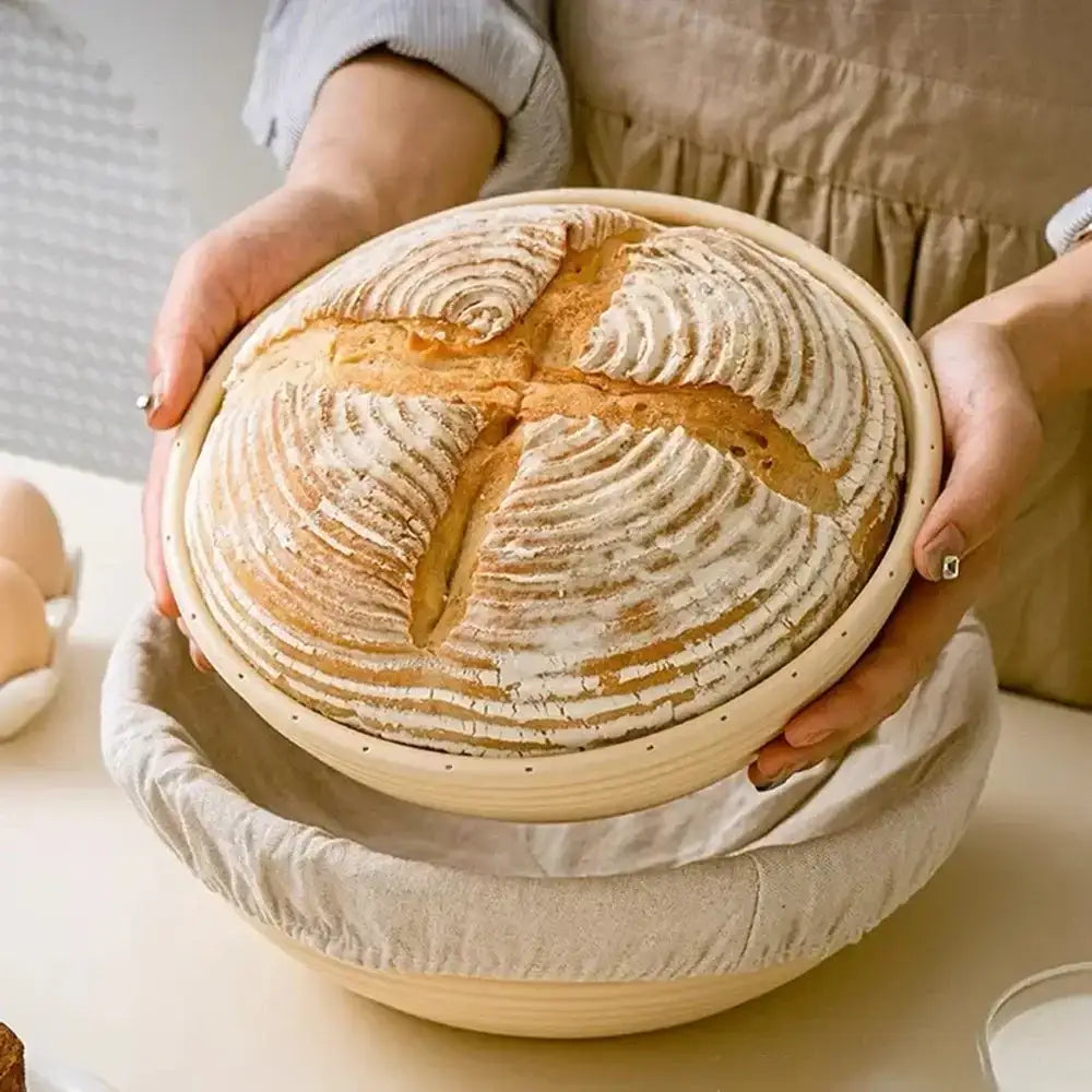 Person holding a loaf of bread in a ceramic dish on a light surface