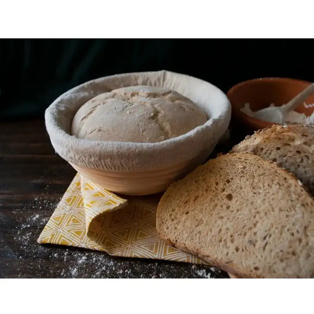 Bread in a rustic ceramic bowl on a wooden surface with a patterned cloth underneath.