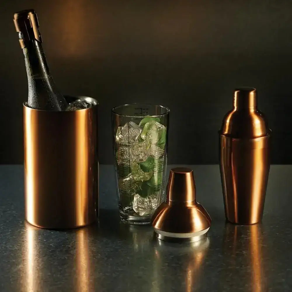 Cocktail shaker, ice bucket, and glass with ice and lime on a dark surface