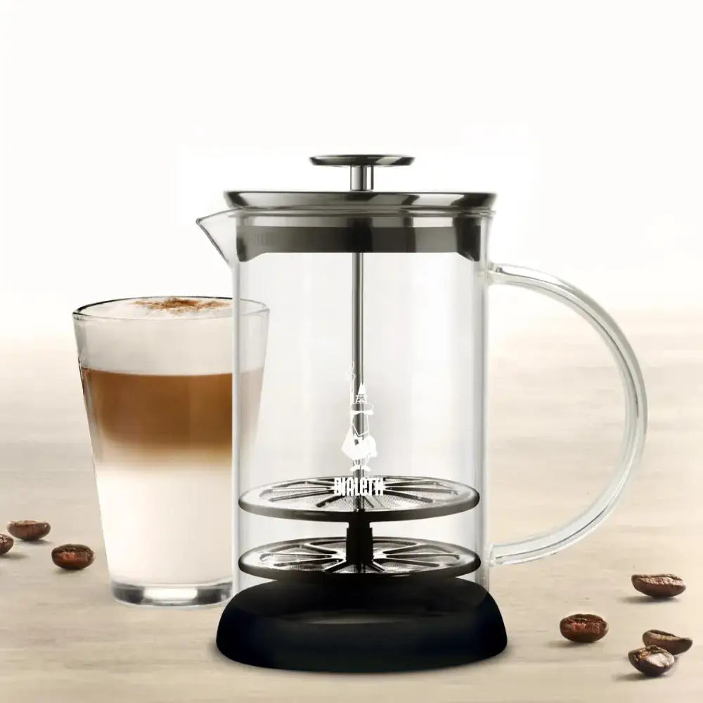 Milk frother with a glass of latte on a wooden surface.