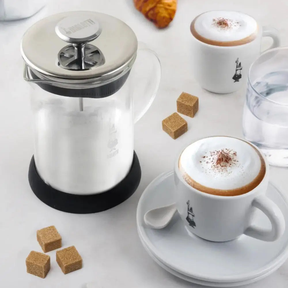 Milk frother, coffee cups, and sugar cubes on a white surface