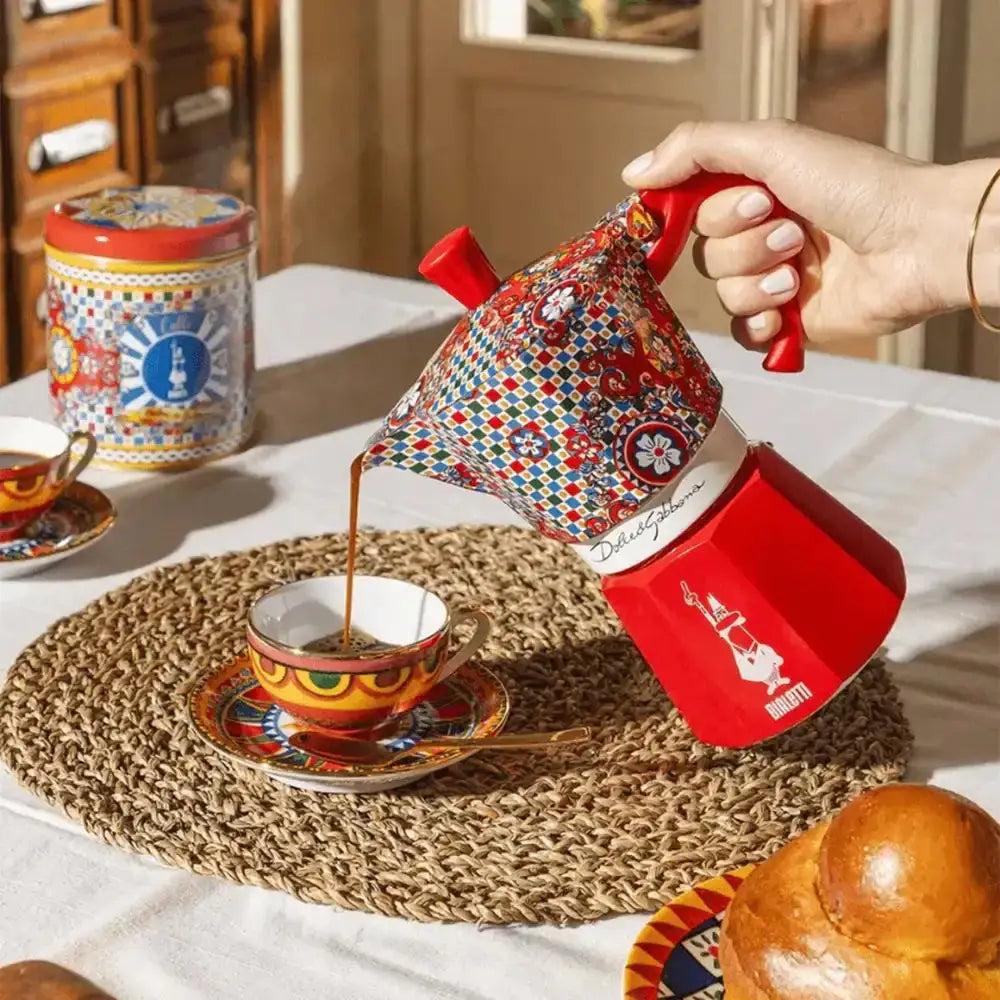 Person pouring coffee from a colorful coffee pot into a cup on a table.