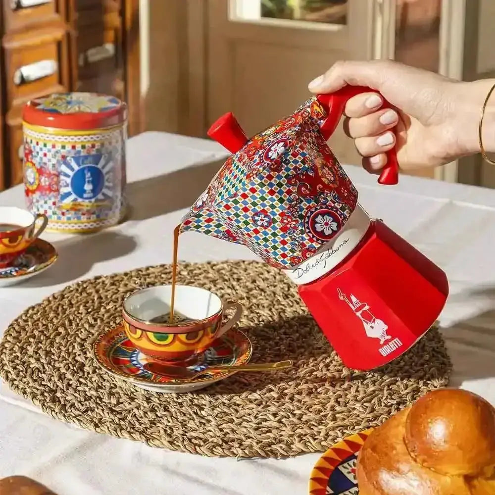 Person pouring coffee from a colorful coffee pot into a cup on a table.