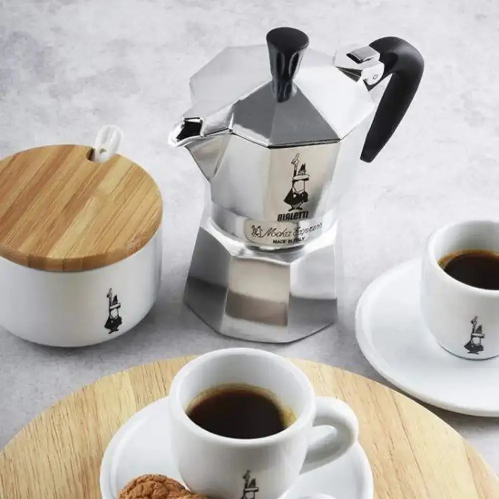 Bialetti Moka Express stovetop espresso maker with coffee cups and sugar jar, premium kitchenware