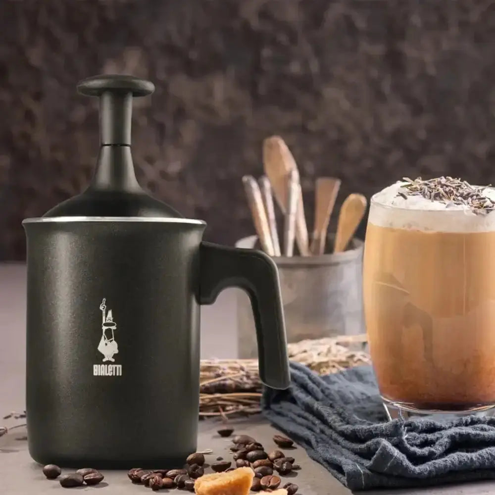 Black coffee press and glass of iced coffee with whipped cream and sprinkles on a wooden surface.