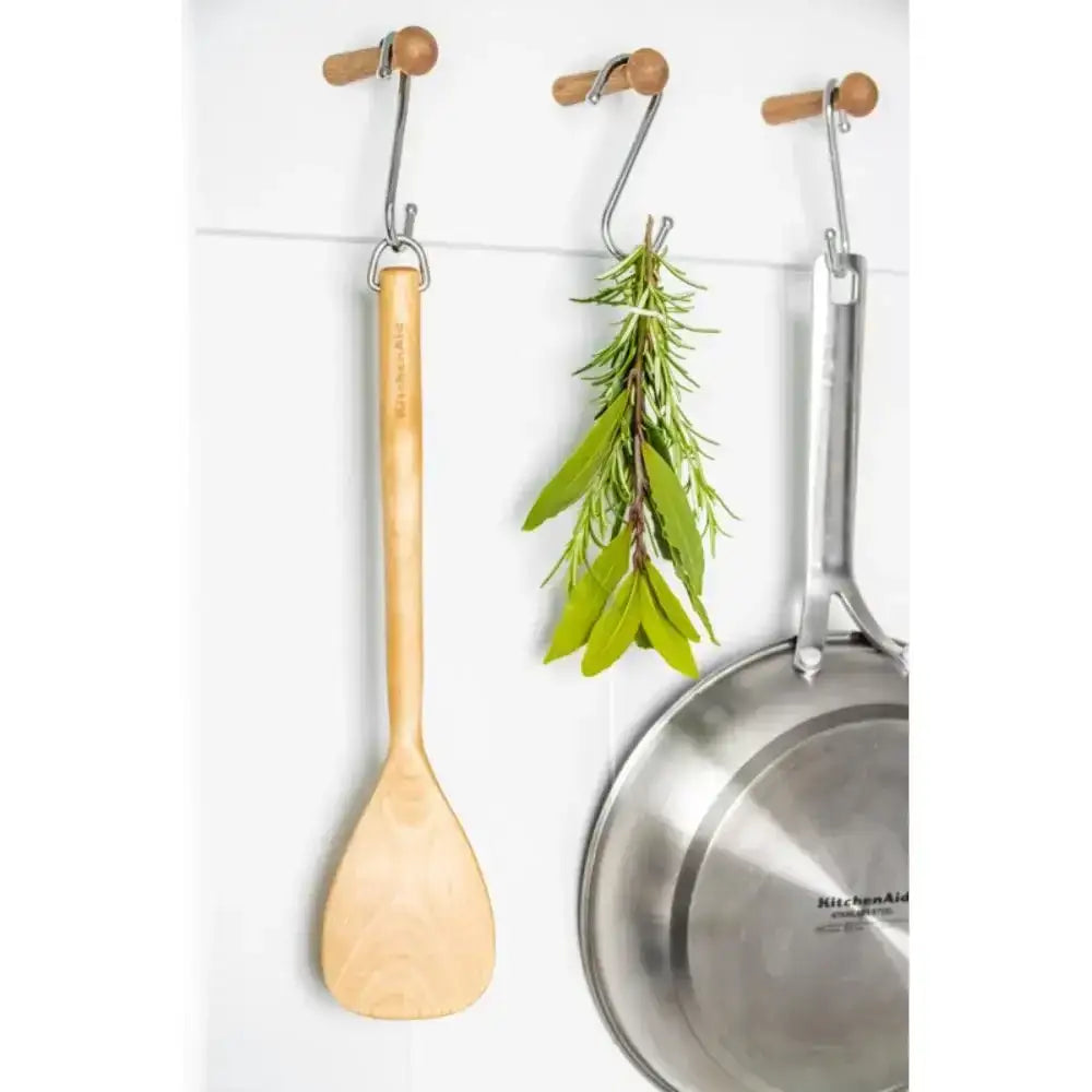 Wooden spoon, metal pan, and herbs hanging on a magnetic strip against a white background