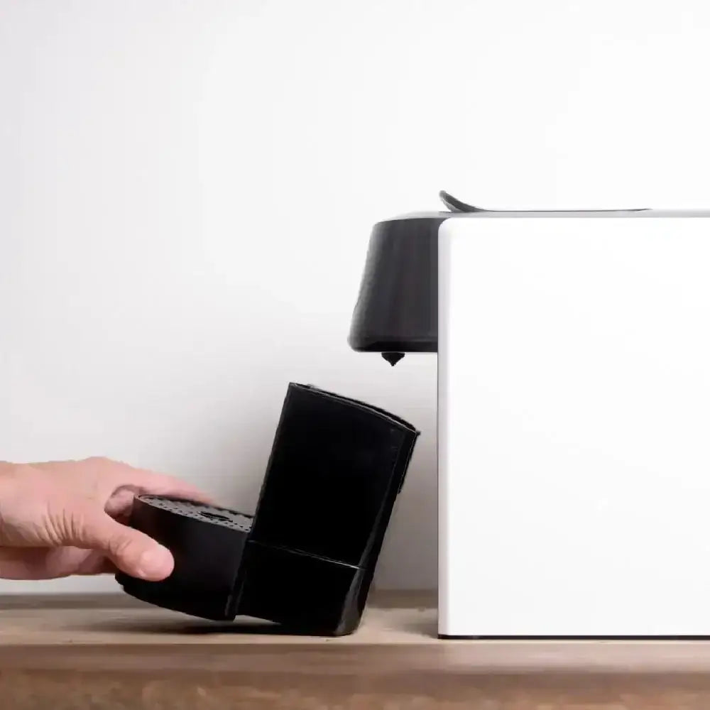 Hand removing drip tray from white capsule coffee machine on wooden counter at Cookin Stores