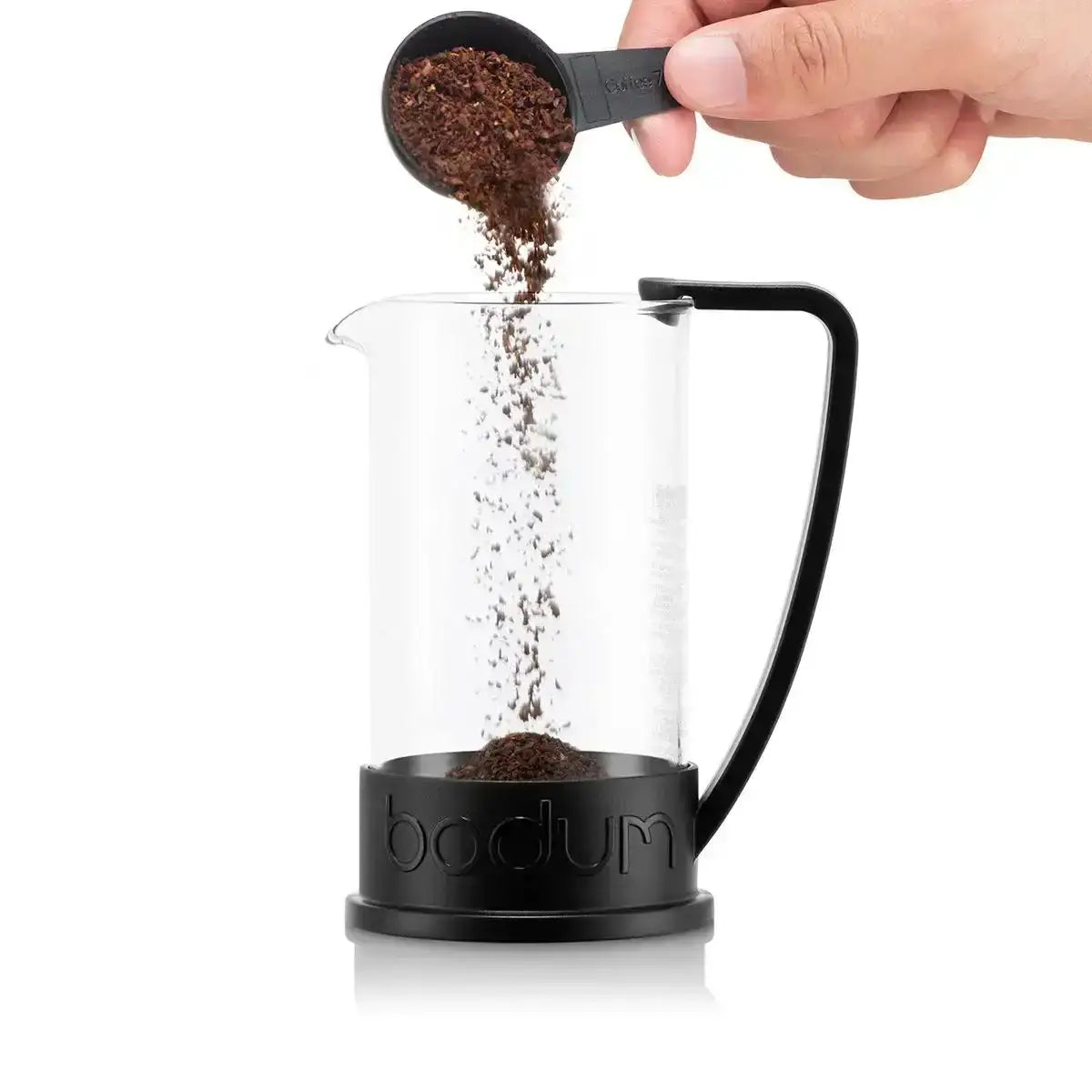 Person pouring coffee grounds into a Bodum coffee maker on a white background
