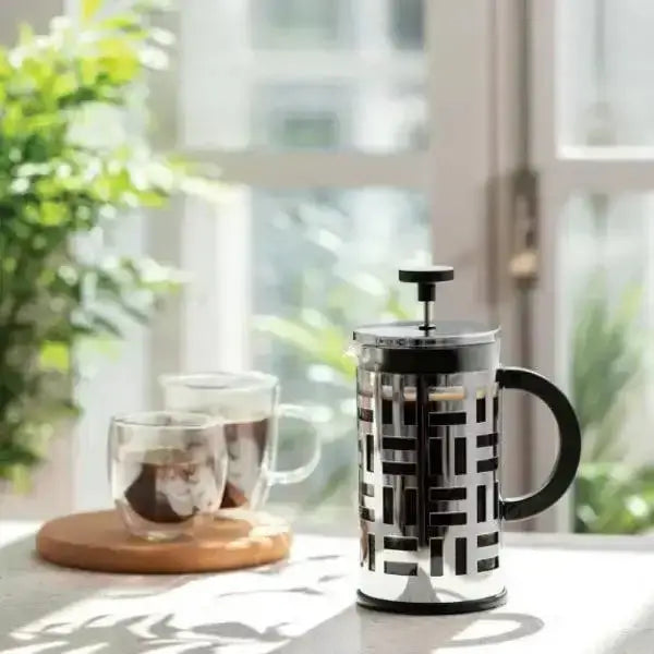 French press coffee maker with geometric pattern on a table with mugs and a plant in the background