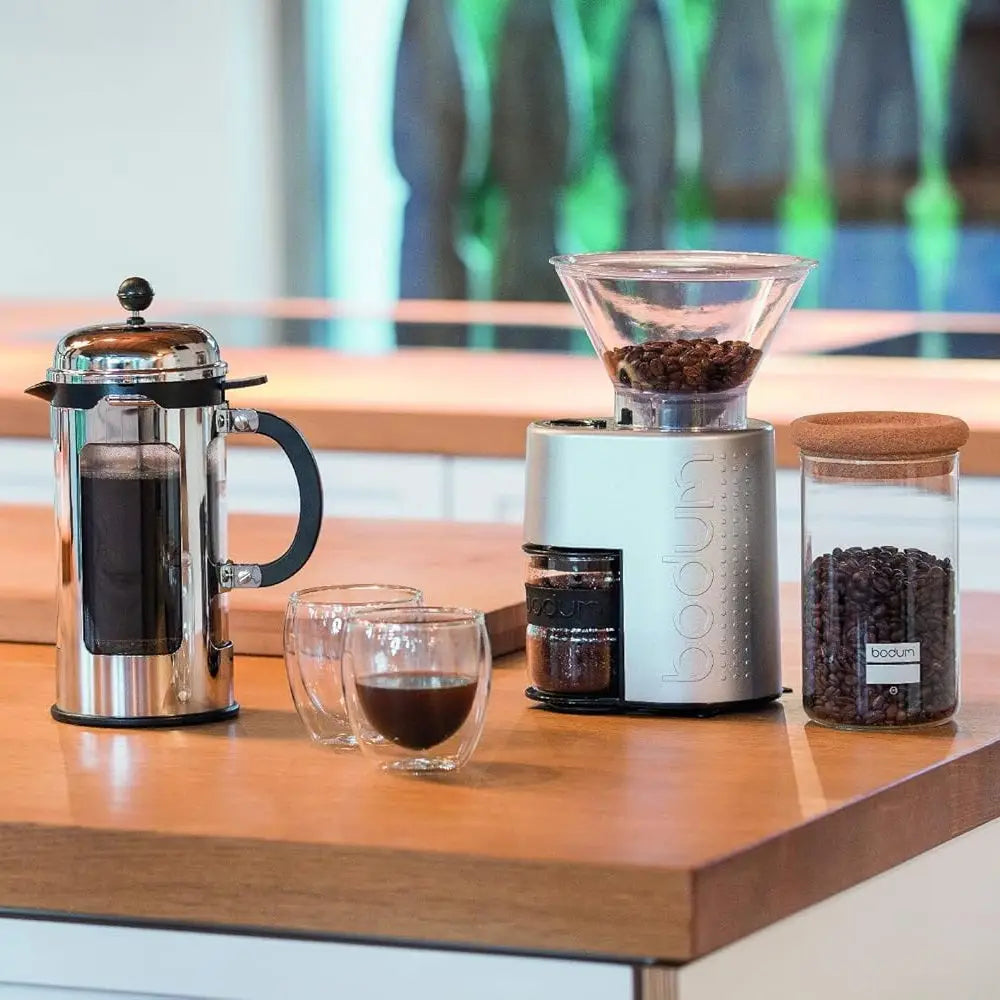 Bodum coffee-making setup with French press, grinder, and beans on a wooden surface.
