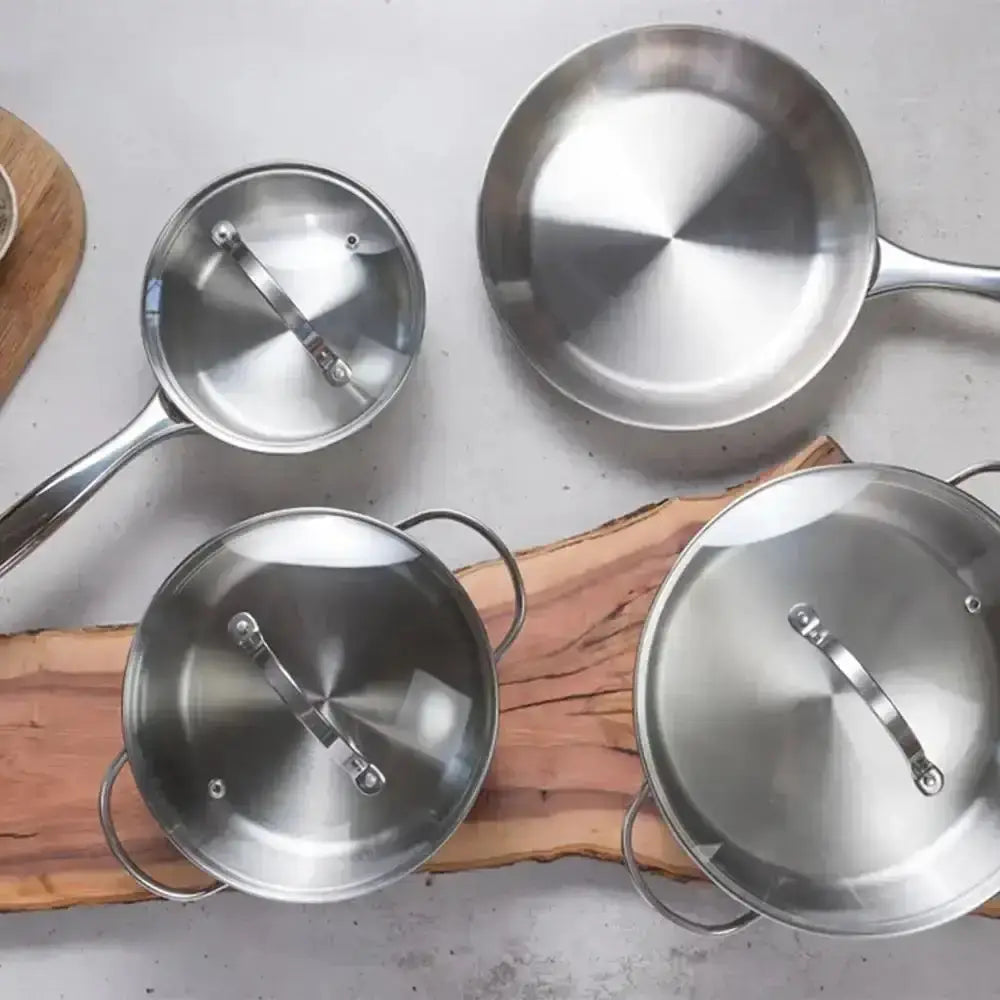 Set of stainless steel cookware including pots and pans on a wooden surface.