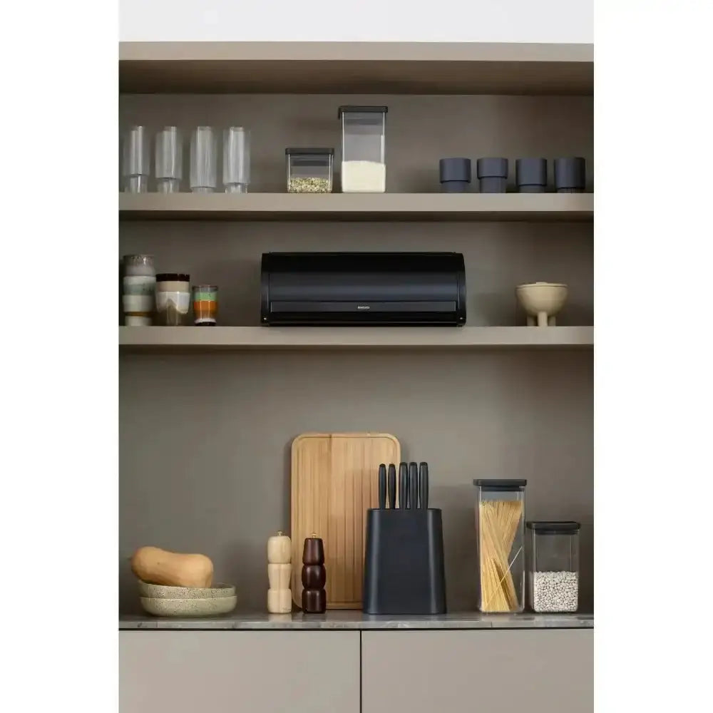Kitchen shelves with various kitchen items including a black knife block, cutting board, and storage containers.