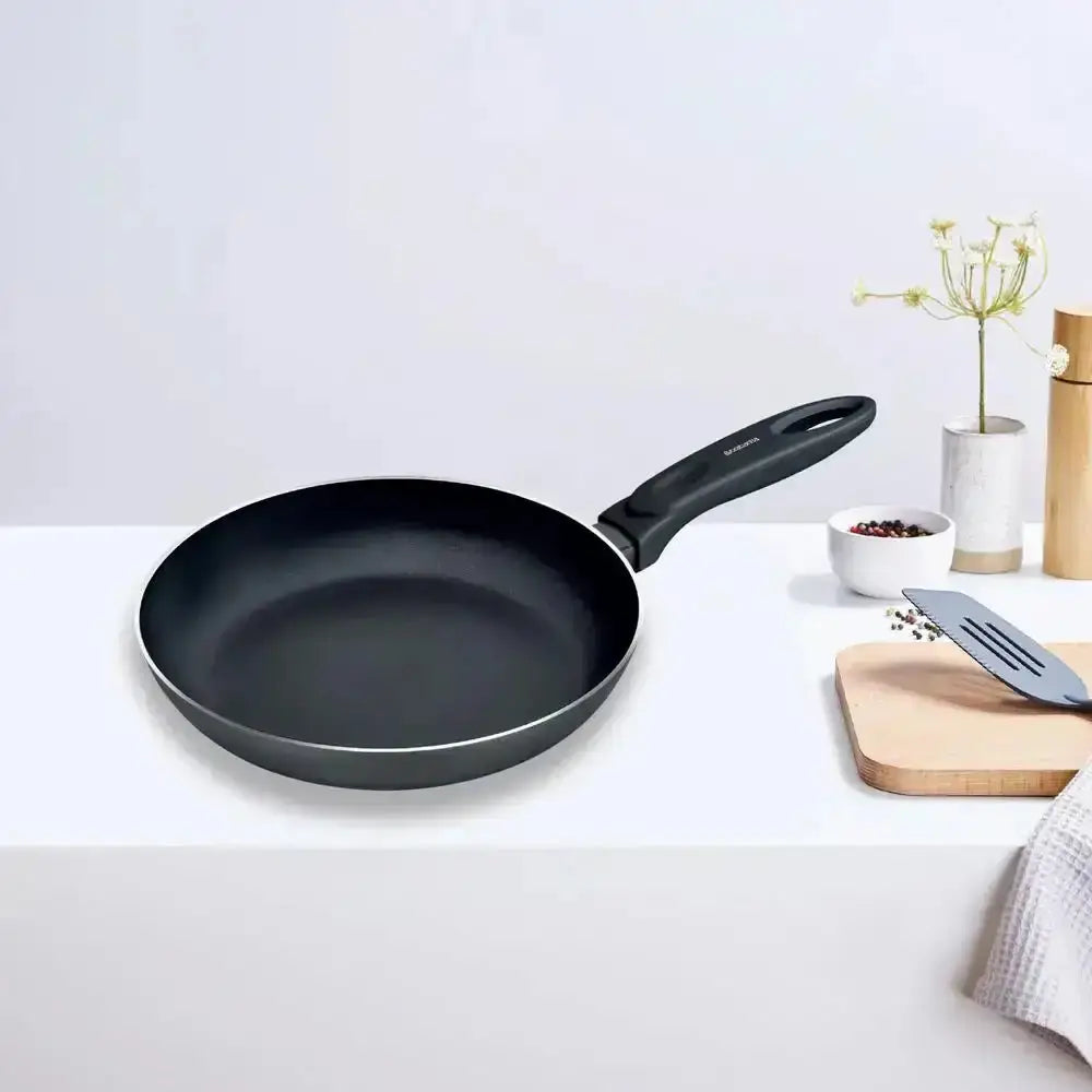 Black frying pan on a white surface with kitchen items in the background