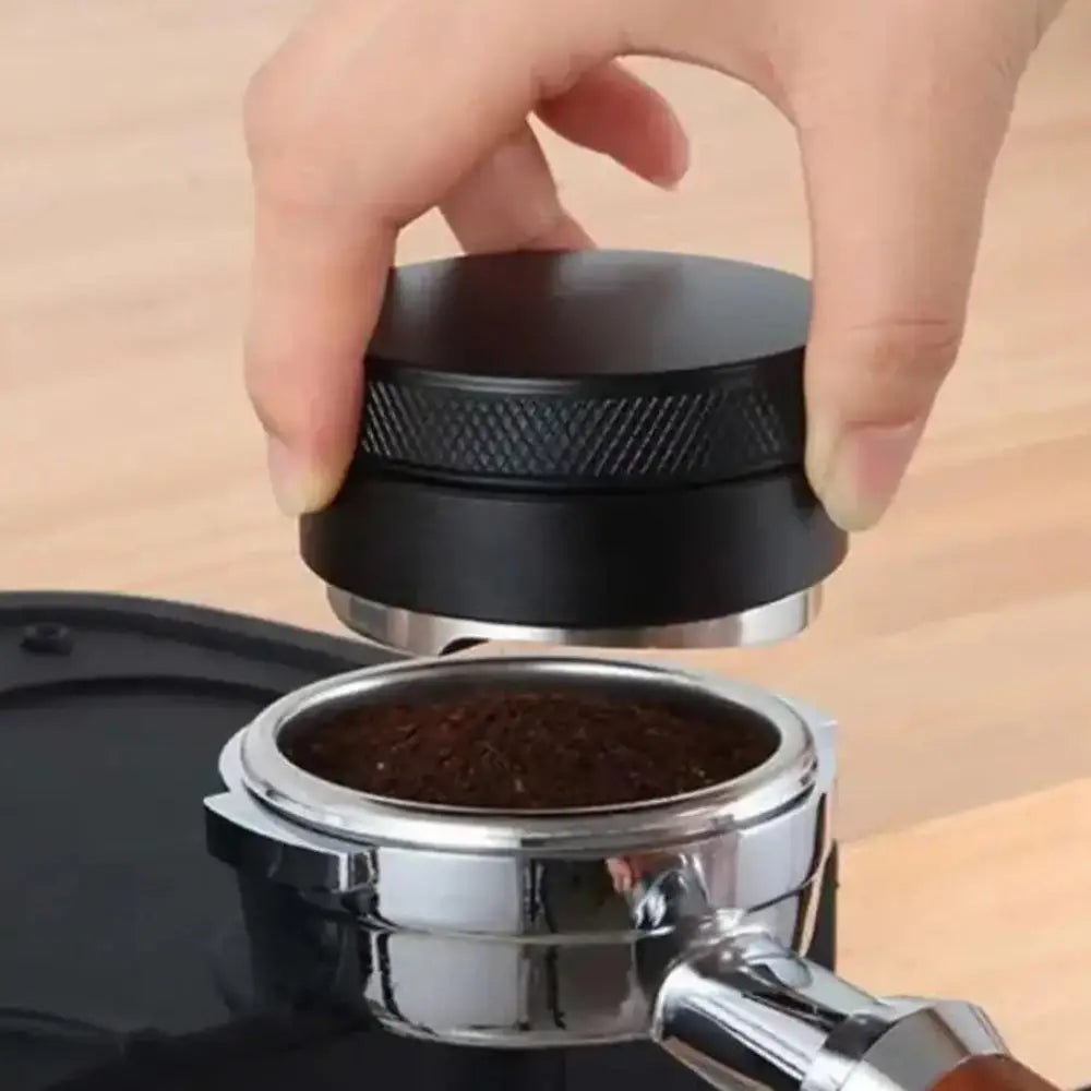 Hand using a coffee tamping tool to compress coffee grounds into a portafilter basket.