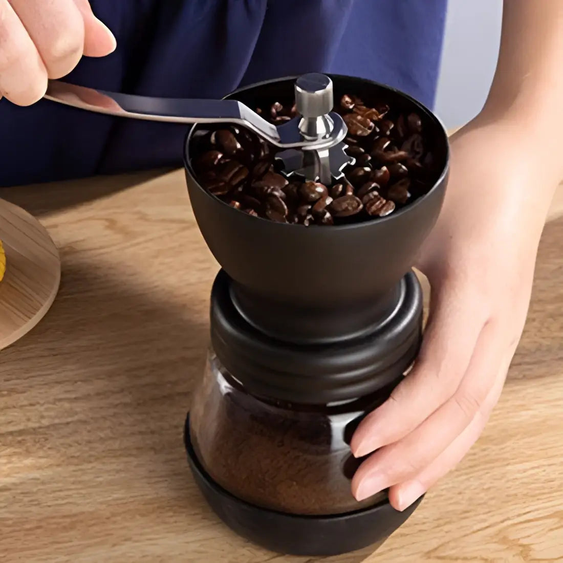 Person using a manual coffee grinder with coffee beans on a wooden table