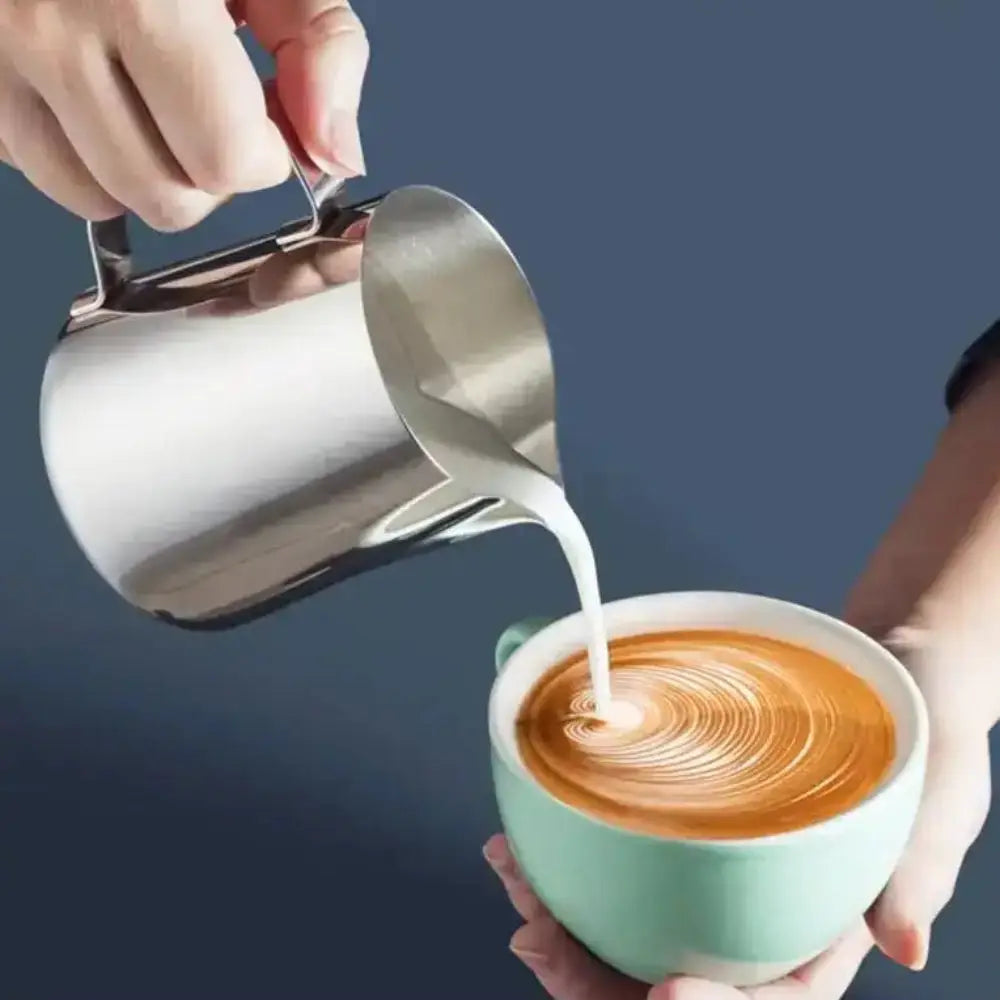 Person pouring milk from a stainless steel pitcher into a cup of coffee with a blue background