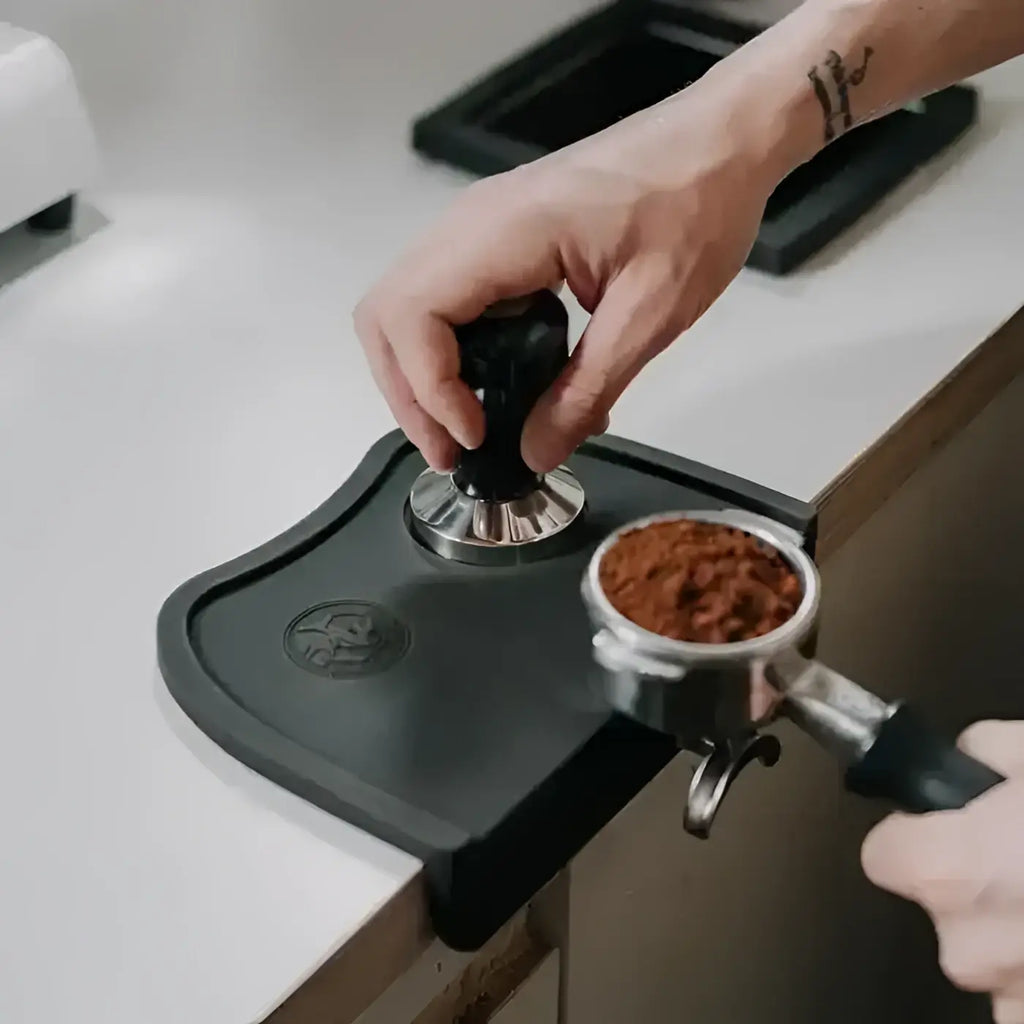 Person using a coffee tamper to press coffee grounds into a portafilter.