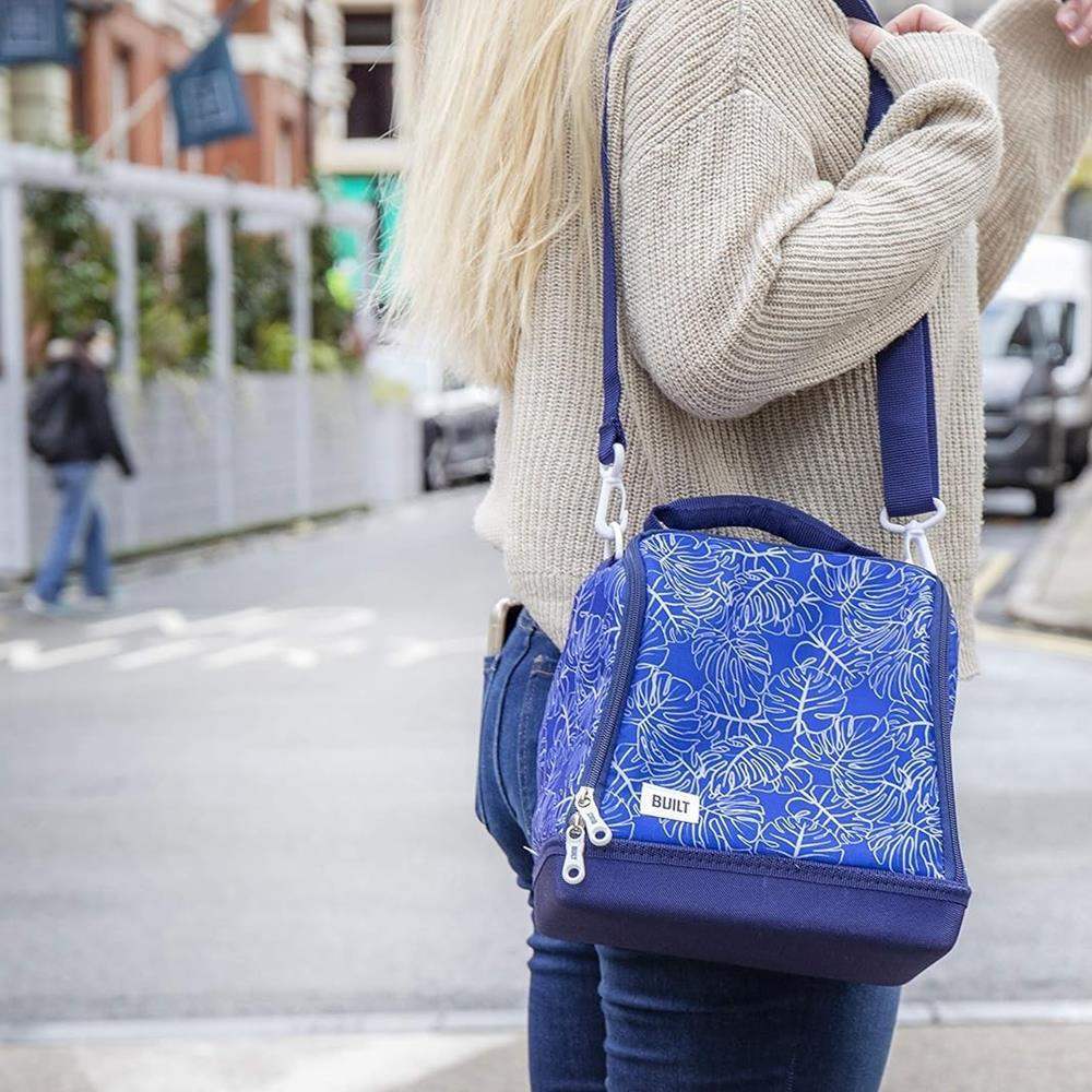 Person wearing a blue backpack with white leaf patterns on a city street.