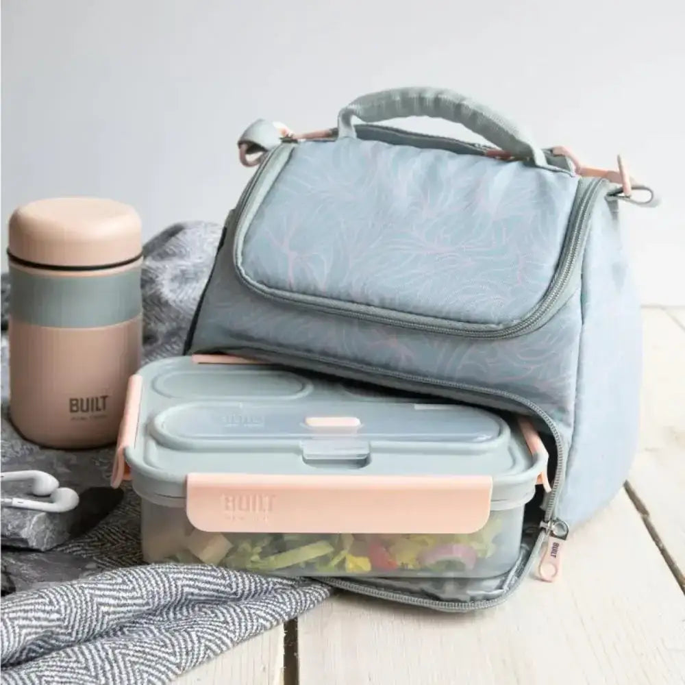 Gray lunch bag, food containers, and a Built brand thermos on a light wooden surface.