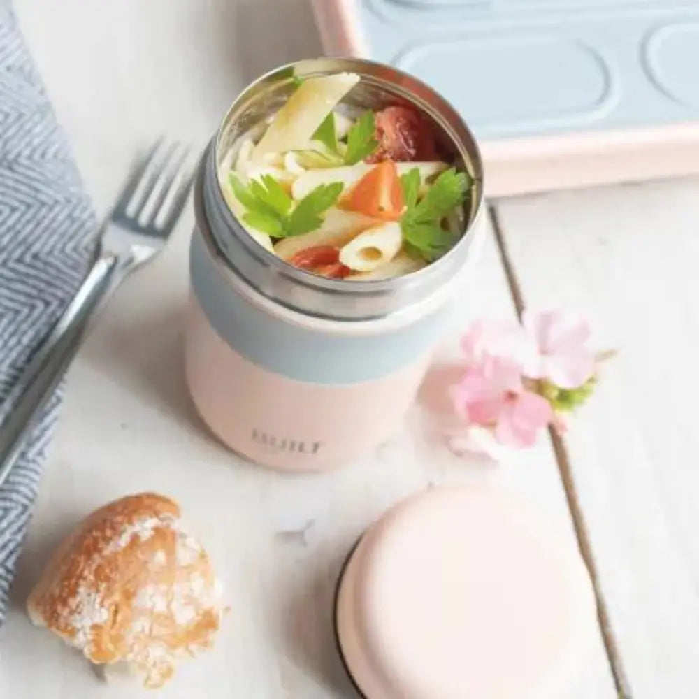 Pink thermos with pasta salad on a white surface with a flower and bread.