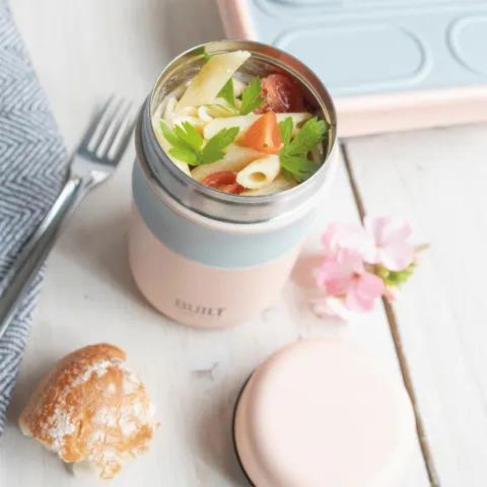 Pink thermos with pasta salad on a white surface with a flower and bread.