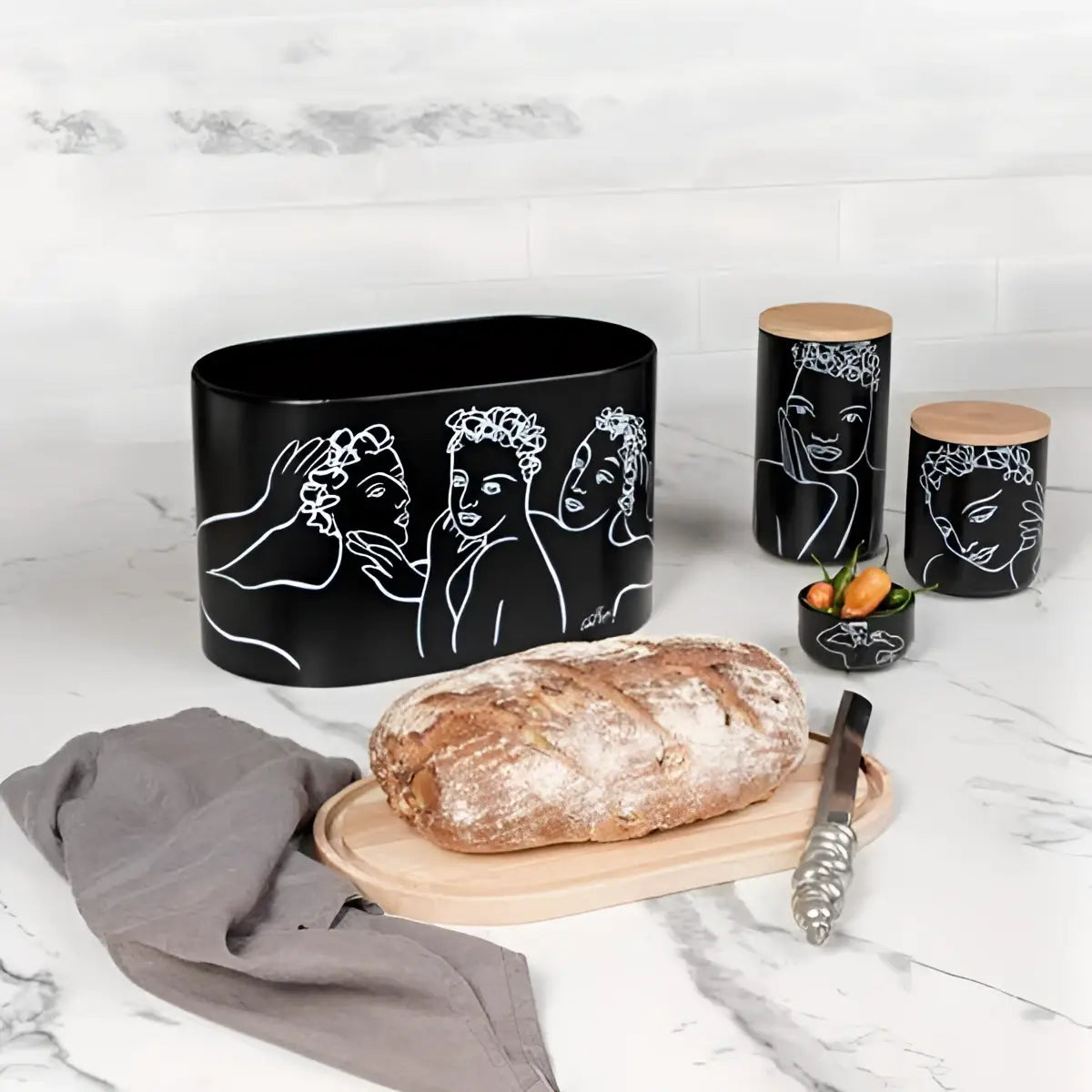 Black ceramic container with artistic designs on a marble surface with bread and a knife.