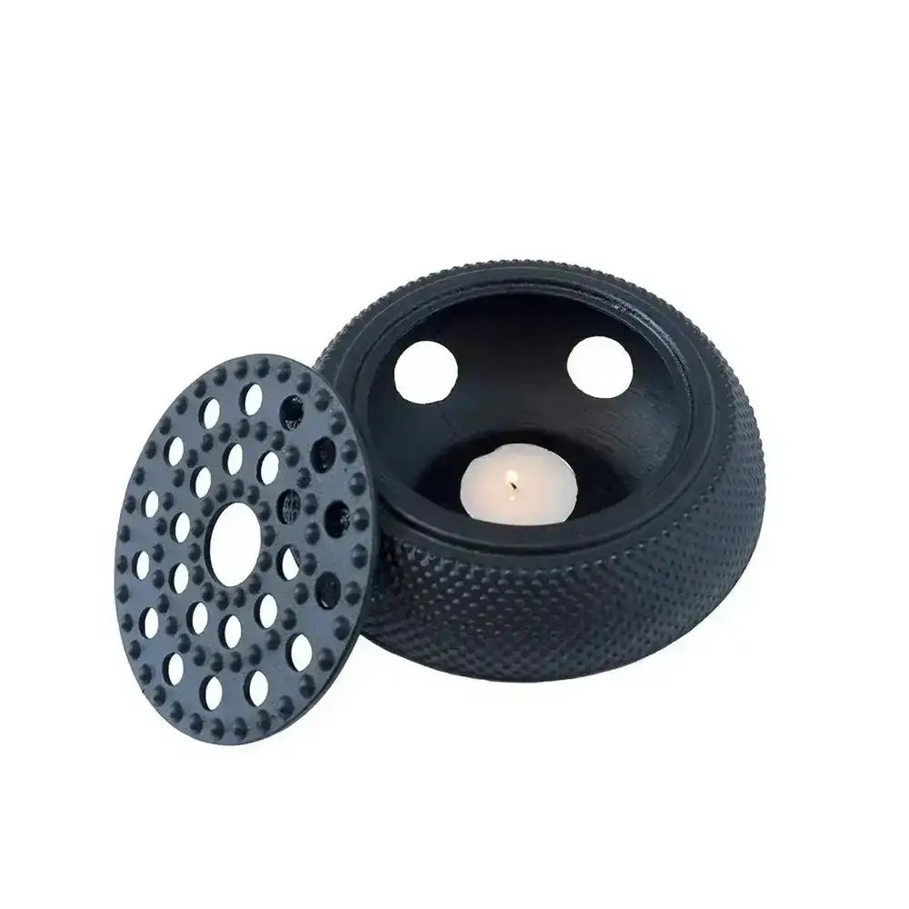 Black tire-shaped candle holder with a lit candle inside on a white background
