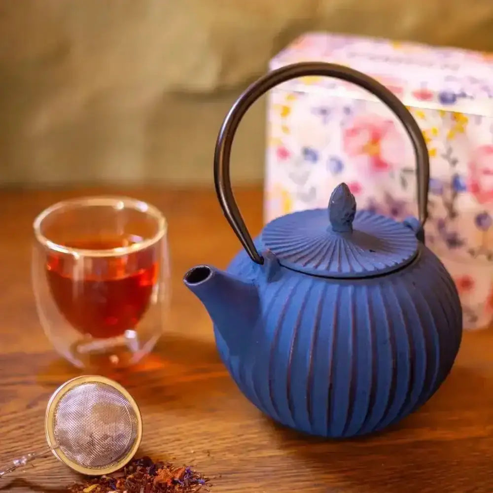 Blue teapot with a glass of tea and tea leaves on a wooden surface.