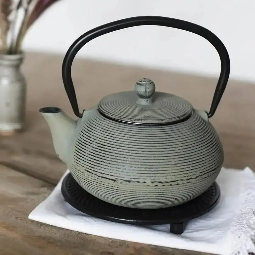 Green ceramic teapot with black handle on a wooden surface