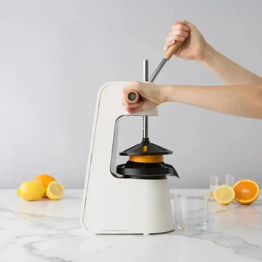 Person using a manual juicer to extract juice from an orange on a marble surface with lemons and glasses.