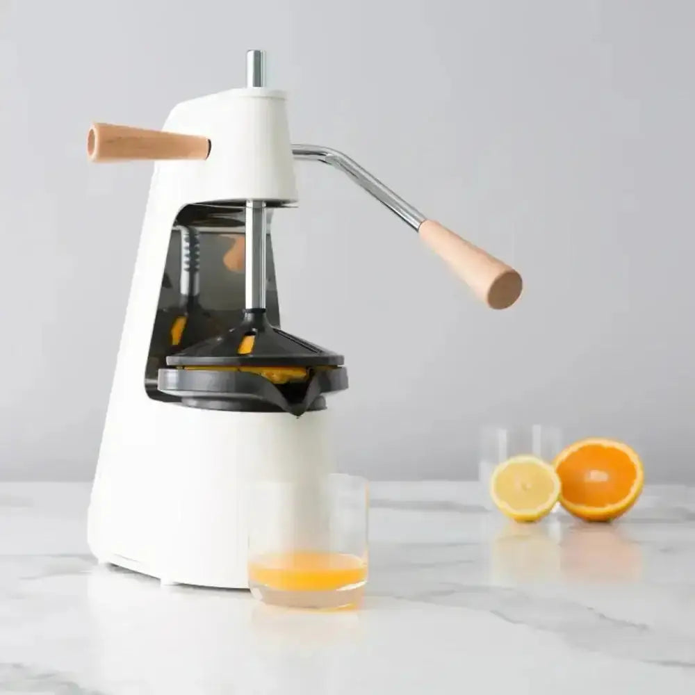 Manual juicer with a glass of orange juice and two oranges on a light gray background
