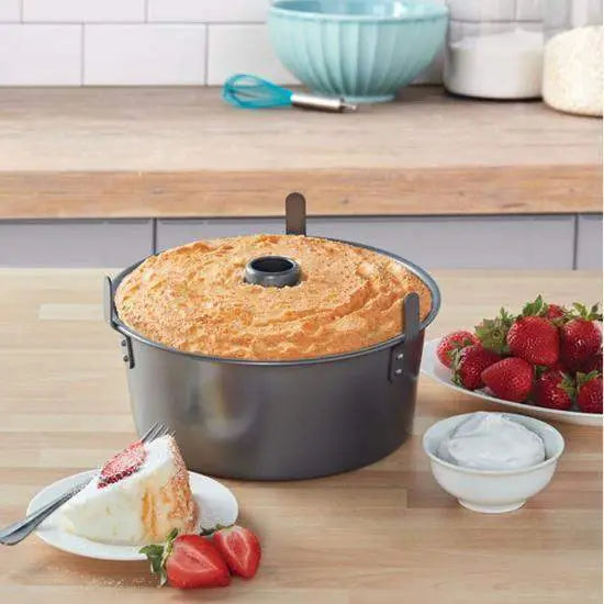 Angel cake in a pan on a kitchen counter with strawberries and a slice of cake.