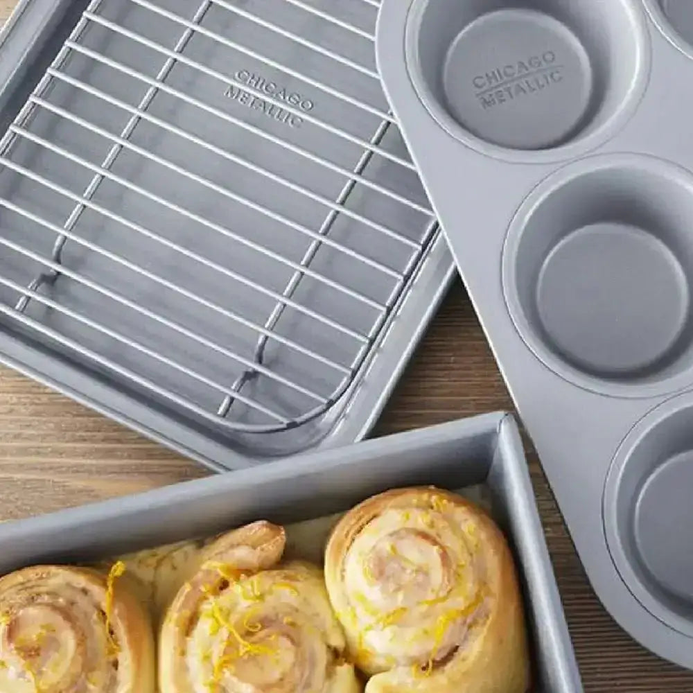 Chicago Metallic non-stick bakeware set with muffin pan, cooling rack, and rolls on wood table