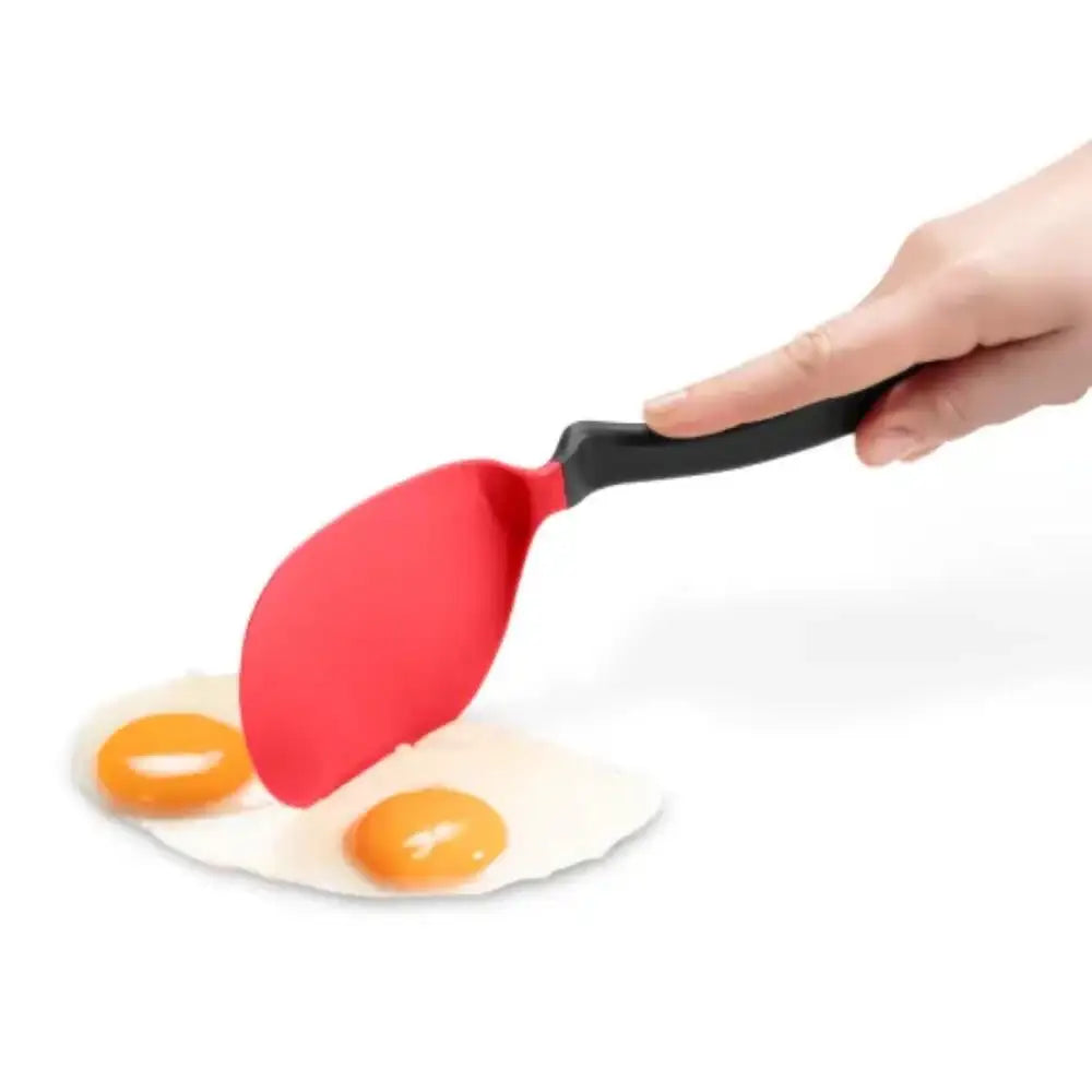 Red spatula with black handle lifting eggs from a white plate on a white background