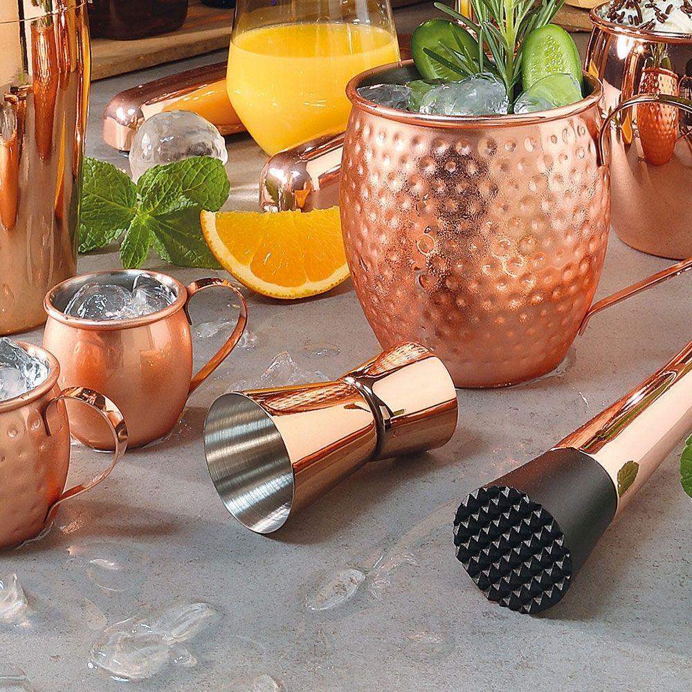 Copper mugs and cocktail shakers on a table with orange slices and ice cubes.