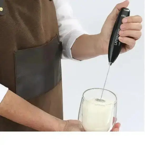 Hand using Cilio Latteforte handheld milk frother to froth milk in a glass, premium kitchenware